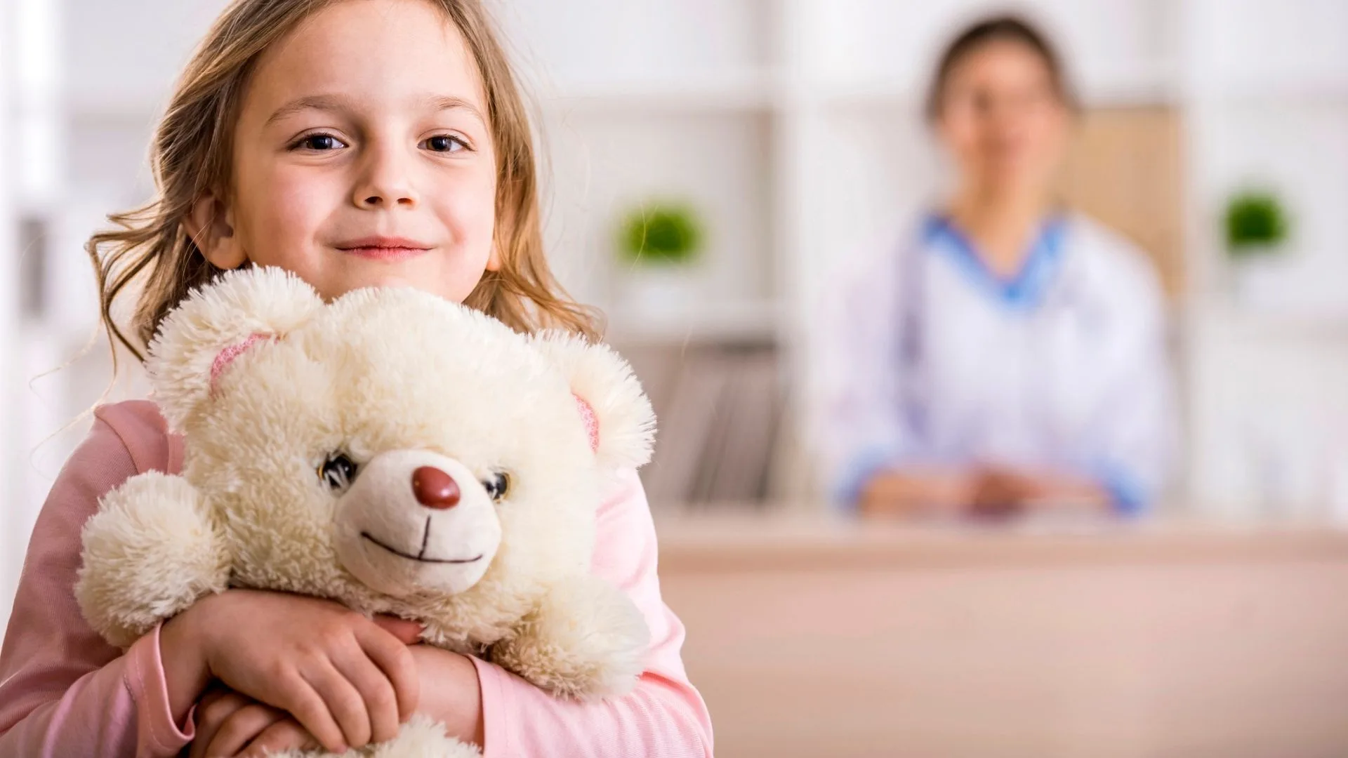 Young girl smiling and holding teddy bear at doctor visit